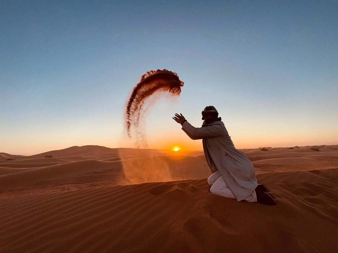 Desert guide throwing sand at sunset in the Merzouga dunes